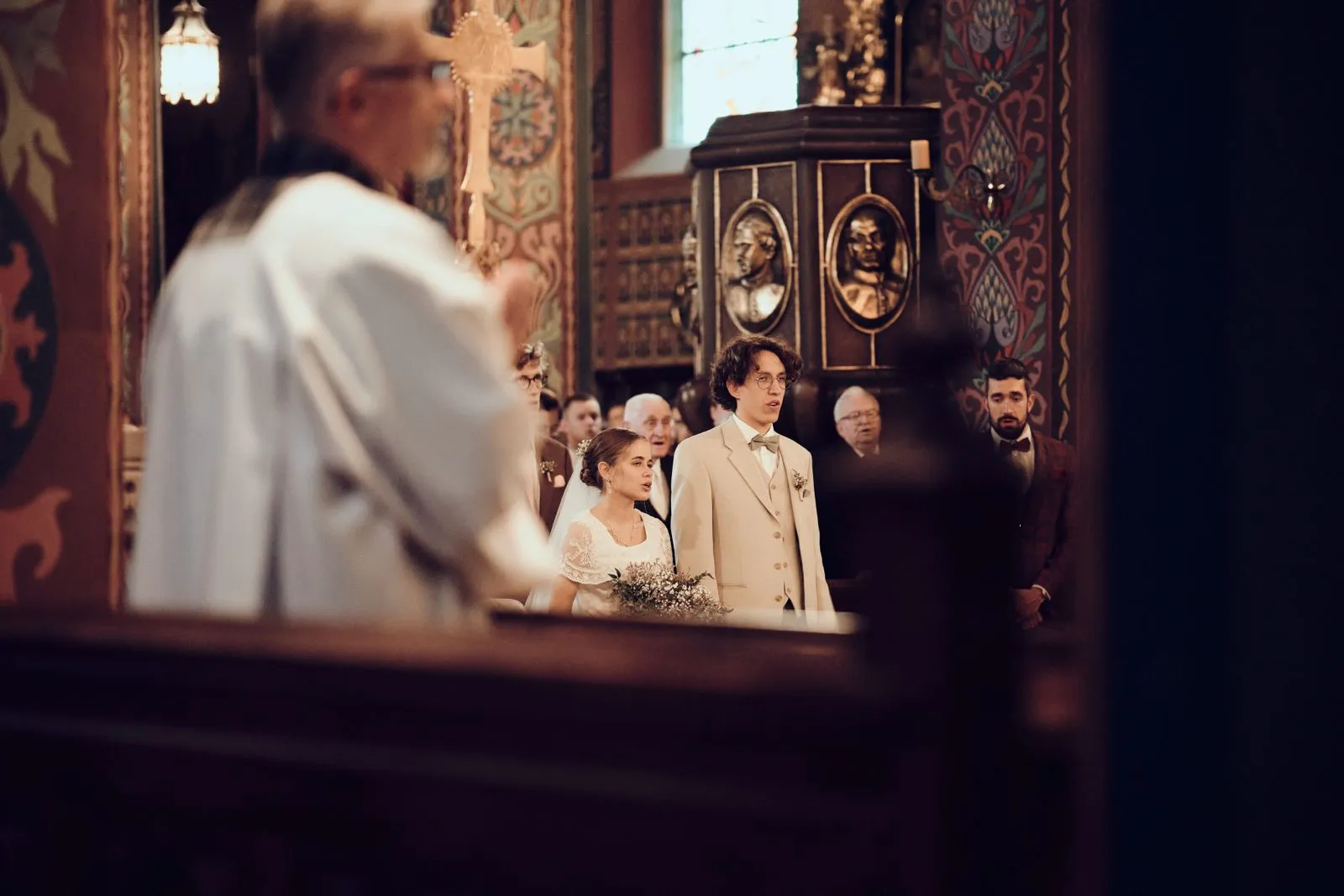 Para młoda podczas ceremonii ślubnej w kościele z gośćmi w tle.