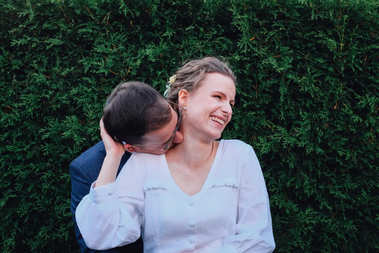 Para w czułych objęciach przed ślubem na tle zielonego żywopłotu, intymny moment miłości.