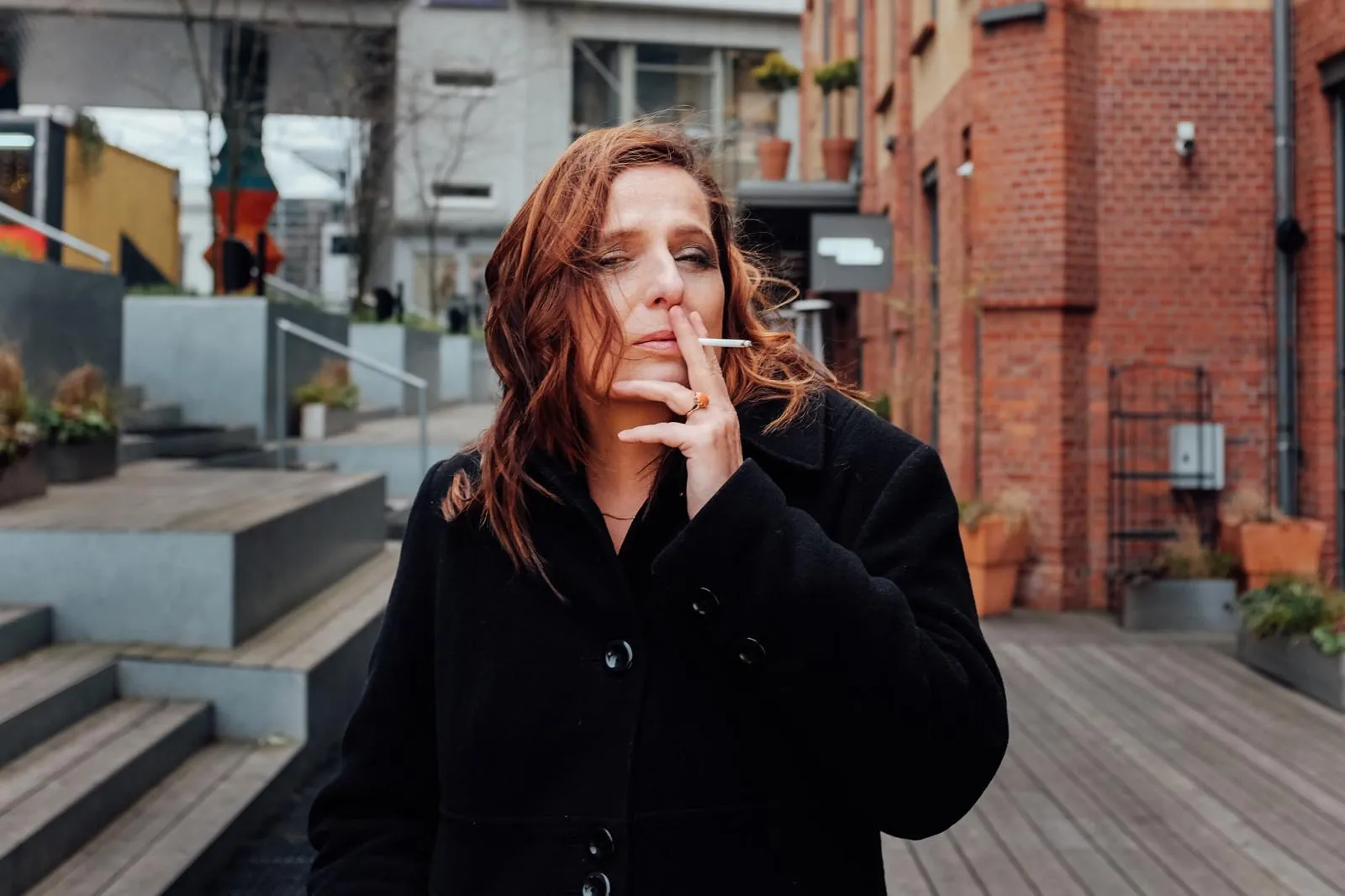 Kobieta w czarnym płaszczu paląca papierosa, portret miejski z charakterem.