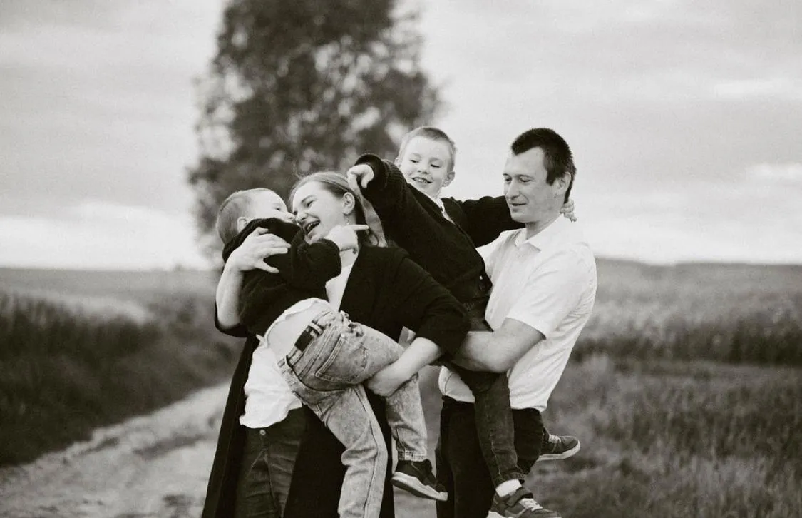 Rodzice trzymają dzieci na rękach, wszyscy śmieją się i przytulają – czuła chwila rodzinna.