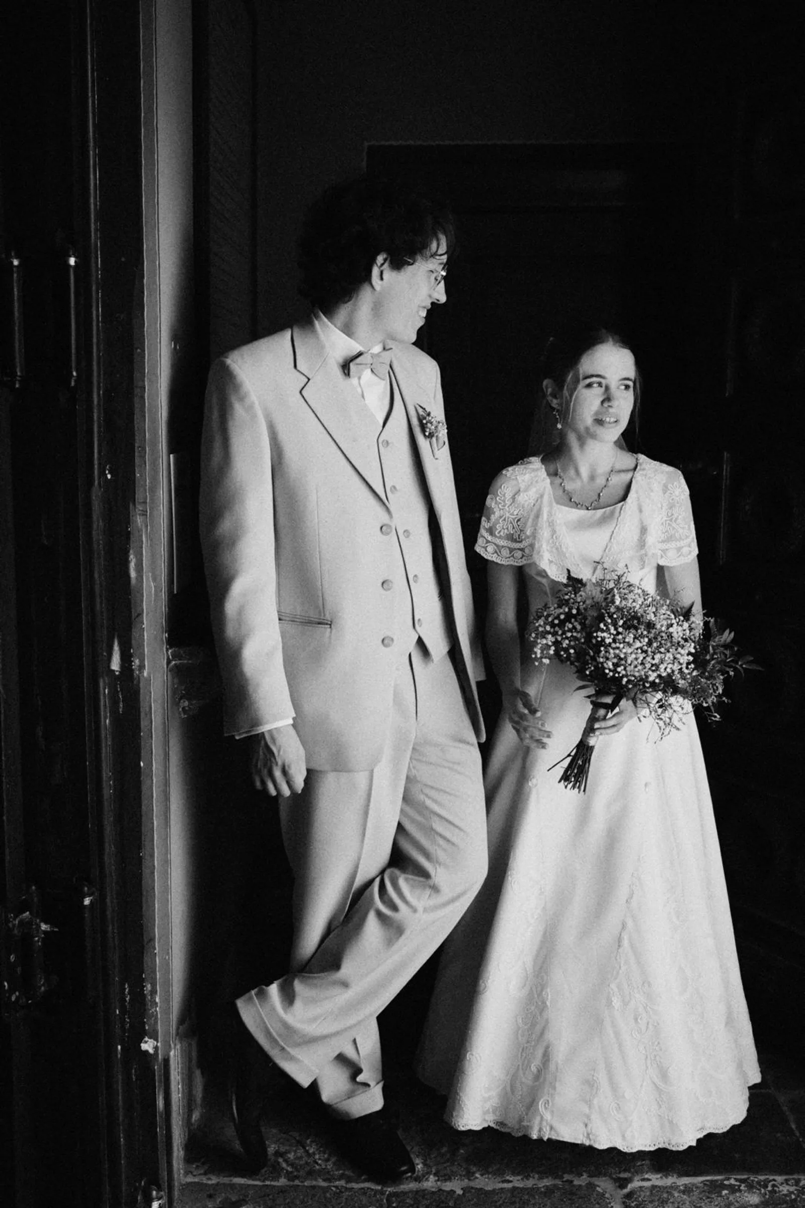 Para młoda stojąca przy drzwiach z bukietem, elegancka sesja ślubna.