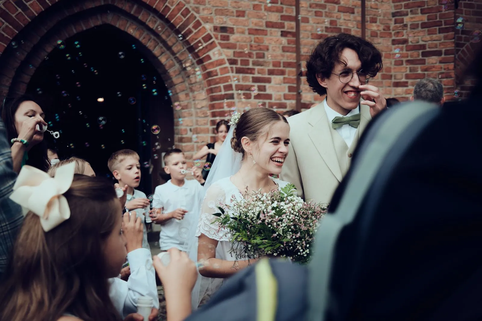 Goście składają życzenia parze młodej z bankami mydlanymi i dzieci w tle.