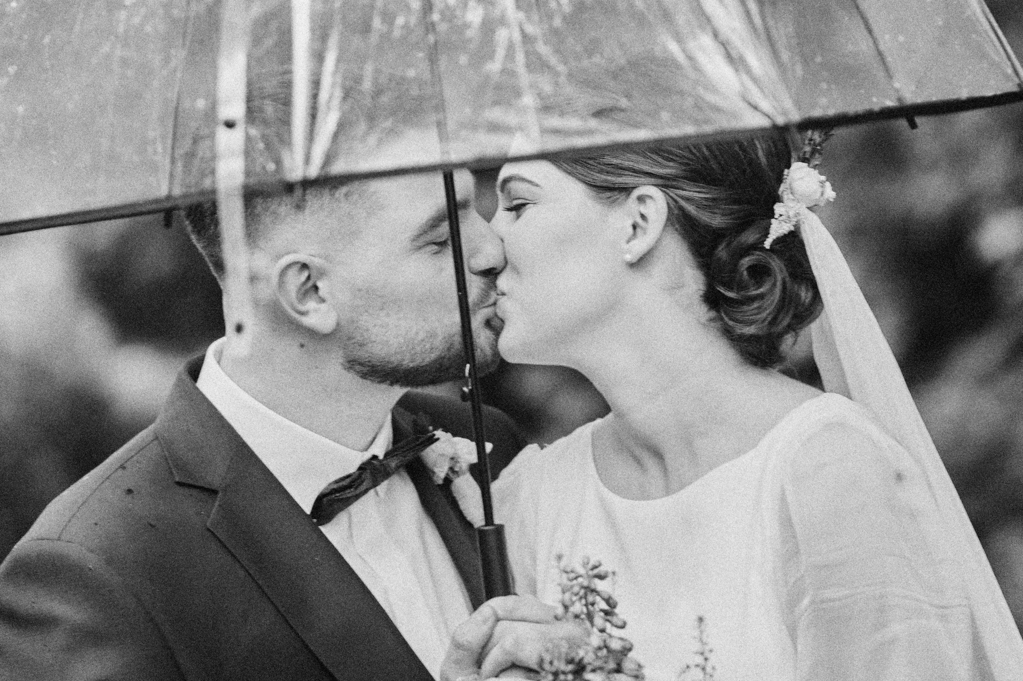 Pocałunek pod parasolem, czarno-biały portret pary młodej.